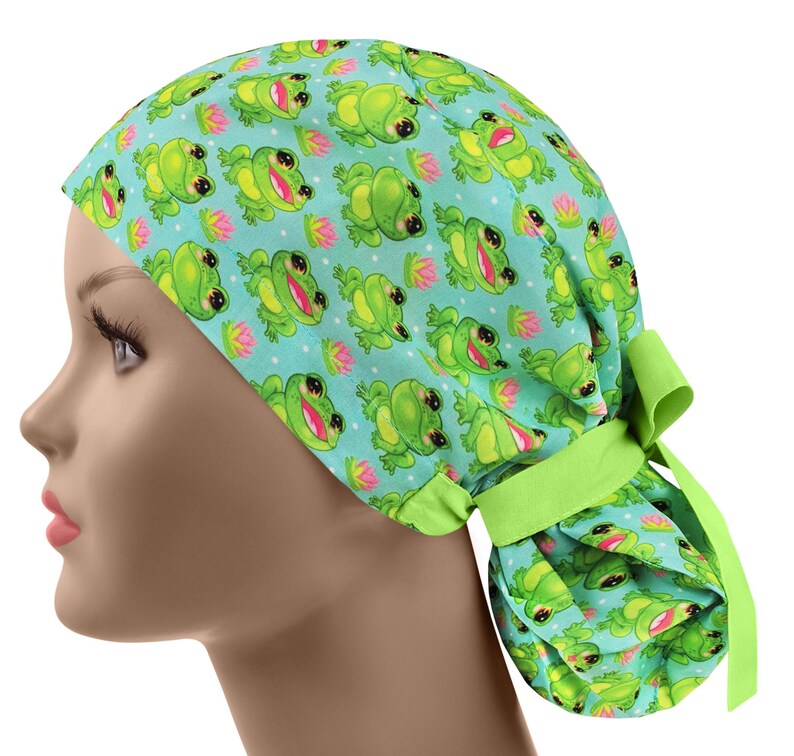 May include: A light blue scrub cap featuring a repeating pattern of smiling green frogs and pink water lilies. The cap has a lime green tie in the back. The cap is designed to be worn on the head.