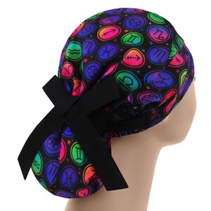 Puede incluir: Un gorro quirúrgico negro con un colorido patrón de signos del zodiaco. El gorro tiene un lazo negro en la parte trasera. El fondo es blanco.