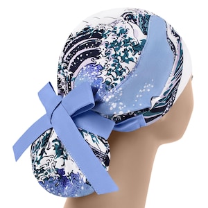 May include: A white scrub cap with a blue wave pattern and a light blue bow. The cap features a design of ocean waves in shades of blue and green. The bow is tied at the back.