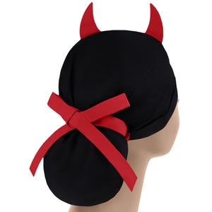 Puede incluir: Un gorro quirúrgico negro con dos cuernos de diablo rojos erguidos en la parte superior. El gorro incluye una cinta de tela roja en la parte posterior, atada en un lazo, que asegura la bolsa de tela negra fruncida para recoger el cabello.