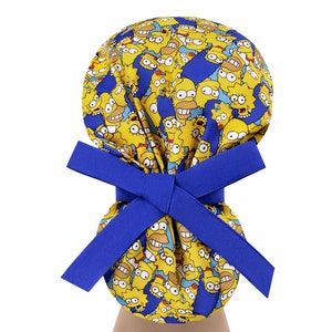 Puede incluir: Un gorro de quir&oacute;fano azul con un patr&oacute;n amarillo y azul de personajes de dibujos animados. El gorro tiene una cinta azul.