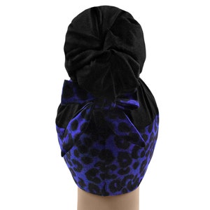 Op de afbeelding: Een zwarte en blauwe turban met een luipaardprint. De turban is bovenop het hoofd in een knot geknoopt.