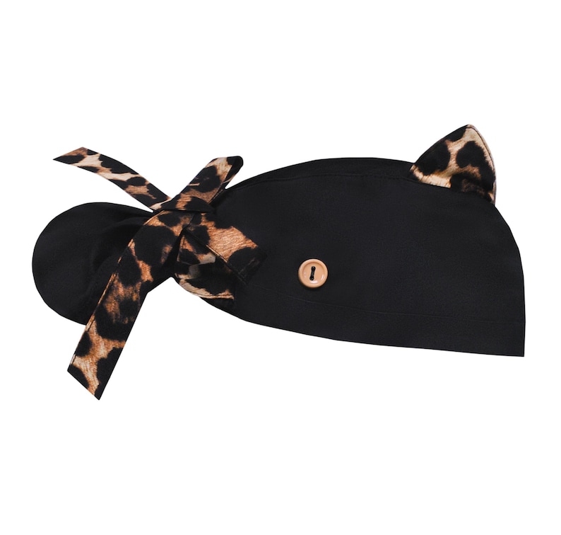 May include: Black scrub cap with a leopard print bow and cat ears. The cap features a wooden button detail and is designed for medical professionals or those in the beauty industry. The leopard print adds a stylish touch to the functional headwear.