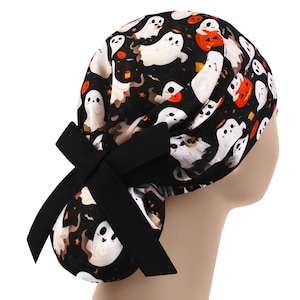 May include: A black Halloween scrub cap featuring a pattern of white ghosts, orange jack-o'-lanterns, and stars. The cap has a large black bow at the back. The fabric is a dark background with a repeating pattern.