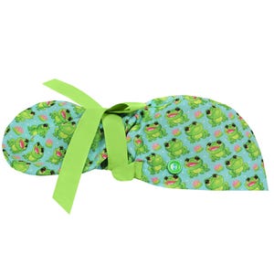 May include: A light blue scrub cap featuring a repeating pattern of smiling green frogs and pink water lilies. The cap has a lime green ribbon for tying and a green button detail.