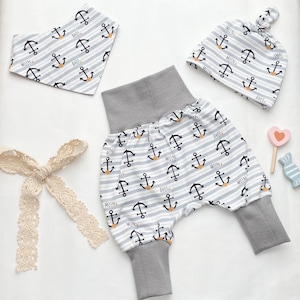 Puede incluir: Un conjunto de ropa de bebé con temática náutica. El conjunto incluye un gorro a rayas gris y blanco con anclas y las palabras "Moin" y "Ahoy", un babero a rayas gris y blanco con anclas y las palabras "Moin" y "Ahoy", y pantalones a rayas gris y blanco con anclas y las palabras "Moin" y "Ahoy".