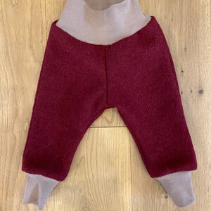 May include: Burgundy wool baby pants with a fold-over waistband and cuffs in a light brown color.
