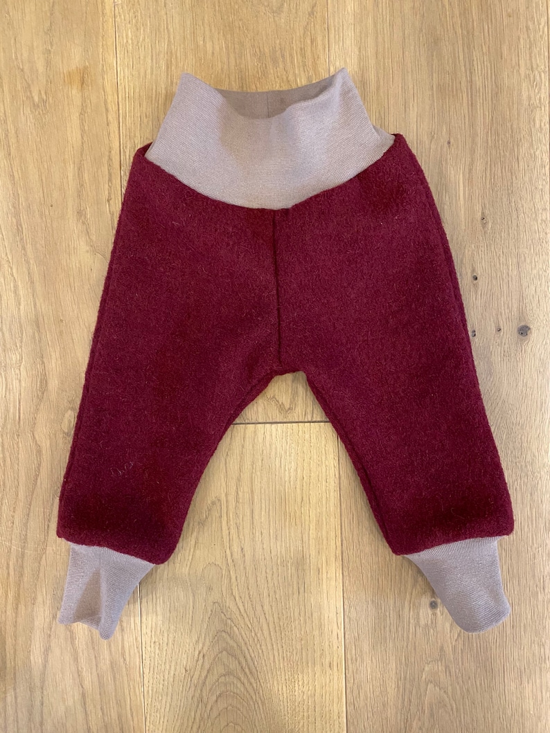 May include: Burgundy wool baby pants with a fold-over waistband and cuffs in a light brown color.