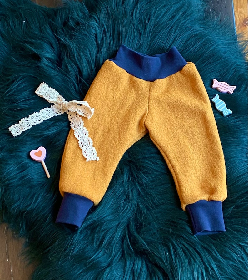 May include: Mustard yellow baby pants with navy blue elastic waistband and cuffs. The pants are made of a soft, fuzzy fabric.