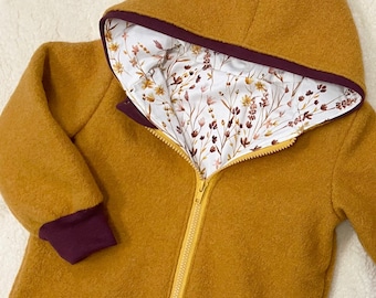 May include: A mustard yellow hooded jacket with a burgundy zipper and trim. The jacket is lined with a white fabric with a floral pattern. The text "Bündchen in Beere Jersey nr 16" is printed on the front of the jacket.