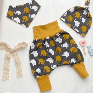 Puede incluir: Un conjunto de ropa para bebé con estampado de elefantes grises y blancos. El conjunto incluye un pantalón harem gris y amarillo mostaza, un gorro gris y blanco con estampado de elefantes con una banda amarilla mostaza y un babero gris y blanco con estampado de elefantes.