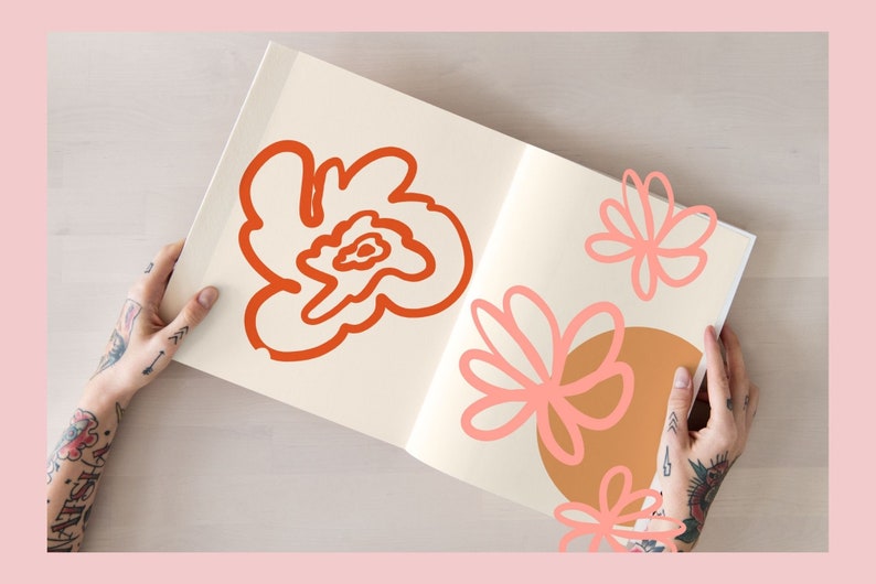 May include: An open sketchbook with hand-drawn illustrations of flowers in orange and pink. The sketchbook is being held by a person with tattoos on their arms.