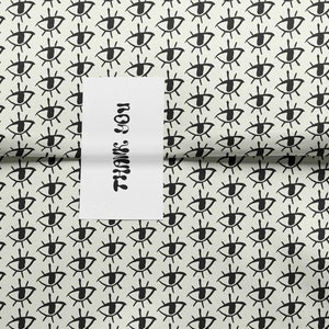 May include: White wrapping paper with a repeating pattern of black stylized eyes. A white card with the text "Thank You" is partially visible.