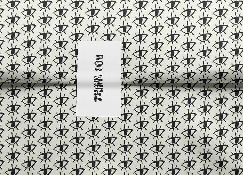 May include: White wrapping paper with a repeating pattern of black stylized eyes. A white card with the text "Thank You" is partially visible.
