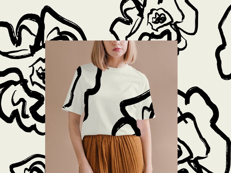 May include: A white t-shirt with a black abstract floral print. The shirt is being modeled by a person with short blonde hair. The background is a light brown color.