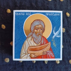 May include: A hand-painted icon of Noah, a biblical figure, holding a wooden ark. The icon is on a blue background with a gold halo around Noah's head. The text "святый Ной" (Saint Noah) is written above the icon, and "праведный" (righteous) is written above the halo.