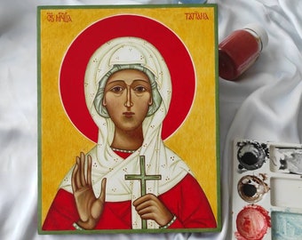 May include: Hand-painted icon of a woman in a white head covering and red robe, holding a cross. The icon is framed in a green border and has a red halo around the woman's head. The icon is titled "Святая Татьяна" in Cyrillic script.