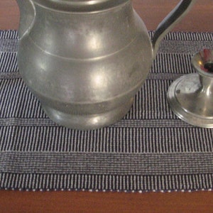 May include: A pewter pitcher and two silver candle holders on a black and white striped table runner.