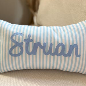 May include: A rectangular cushion with a light blue and white striped design. The name "Struan" is stitched in light blue cursive lettering across the centre. The cushion is placed on a neutral-toned surface.