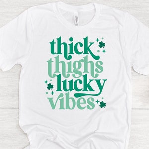 May include: White t-shirt with green text that reads "thick thighs lucky vibes" with shamrock accents.