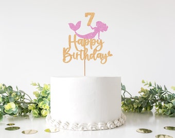 May include: Gold glitter cake topper with a pink glitter mermaid holding the number 7 and the words "Happy Birthday".