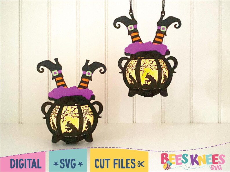 May include: Two black witch legs dangle from a hanging cauldron with a purple rim. The cauldron has a yellow glow inside and a silhouette of a witch stirring a pot. The background is a white wood panel.