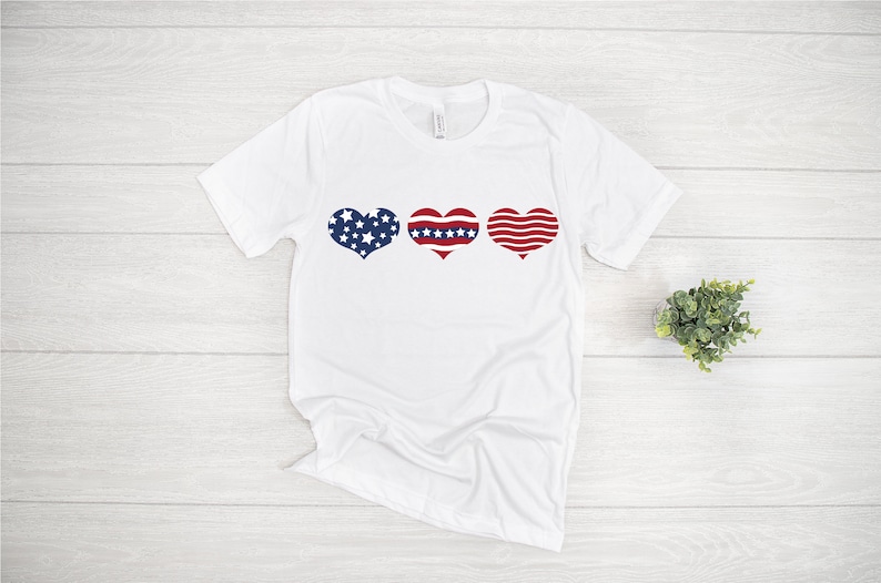May include: White t-shirt with three red, white, and blue hearts in a row. The hearts are patterned with stars and stripes.