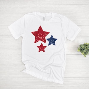 May include: White t-shirt with a red, white, and blue star design. The stars are distressed and have a vintage look.