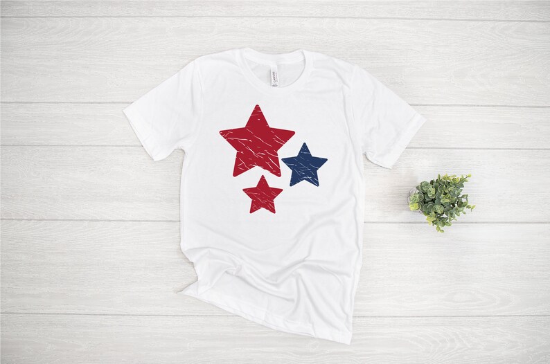 May include: White t-shirt with a red, white, and blue star design. The stars are distressed and have a vintage look.