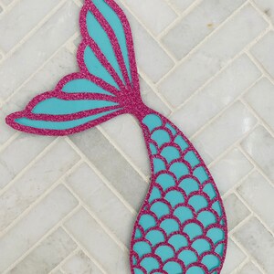 May include: A turquoise mermaid tail cutout with pink glitter. The tail has a scale pattern and a fin.