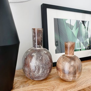 May include: Two wooden vases, one with a white and brown wood grain pattern and the other with a brown wood grain pattern, sitting on a wooden surface.