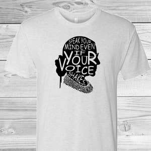 May include: A white t-shirt with a black silhouette of Ruth Bader Ginsburg and the text "Speak your mind even if your voice shakes."
