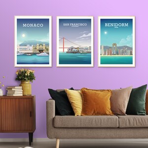 May include: Three framed city skyline posters with a light purple wall in the background. The posters are of Monaco, San Francisco, and Benidorm. A couch with pillows is in the foreground.