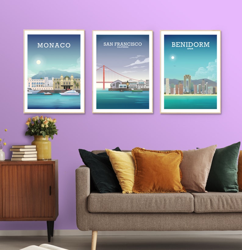 May include: Three framed city skyline posters with a light purple wall in the background. The posters are of Monaco, San Francisco, and Benidorm. A couch with pillows is in the foreground.