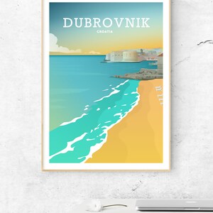 May include: A framed travel poster of Dubrovnik, Croatia, featuring a beach with turquoise water and a sandy shore. The poster has a minimalist design with the city name in white and a light blue and yellow sky.
