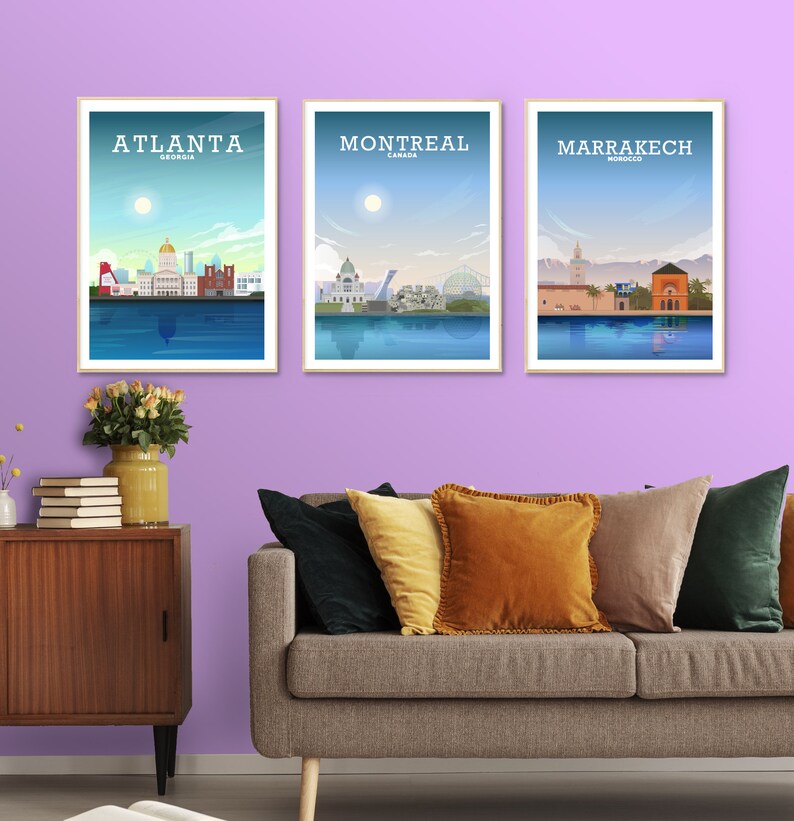 May include: Three framed city skyline posters with a light blue background and white text. The posters are titled "Atlanta, Georgia", "Montreal, Canada", and "Marrakech, Morocco". The posters are hanging on a light purple wall above a gray couch with pillows.