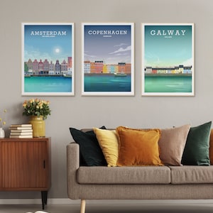 K&ouml;nnte beinhalten: Drei gerahmte Stadtbild-Poster mit den Namen "Amsterdam", "Kopenhagen" und "Galway" darauf gedruckt. Die Poster h&auml;ngen an einer hellgrauen Wand &uuml;ber einem braunen Sofa mit bunten Kissen.
