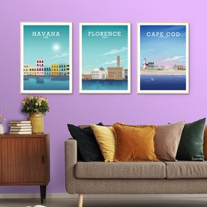 May include: Three framed prints of cityscapes with the names "HAVANA CUBA", "FLORENCE ITALY", and "CAPE COD UNITED STATES" printed below each image. The prints are hanging on a light purple wall above a brown couch with multiple pillows.