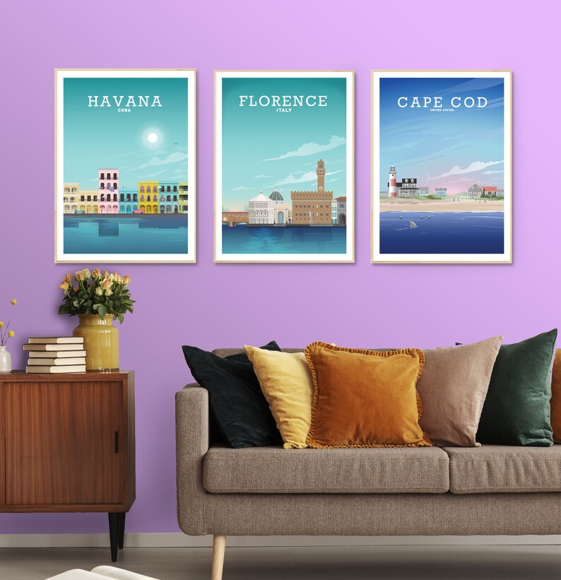 May include: Three framed prints of cityscapes with the names "HAVANA CUBA", "FLORENCE ITALY", and "CAPE COD UNITED STATES" printed below each image. The prints are hanging on a light purple wall above a brown couch with multiple pillows.