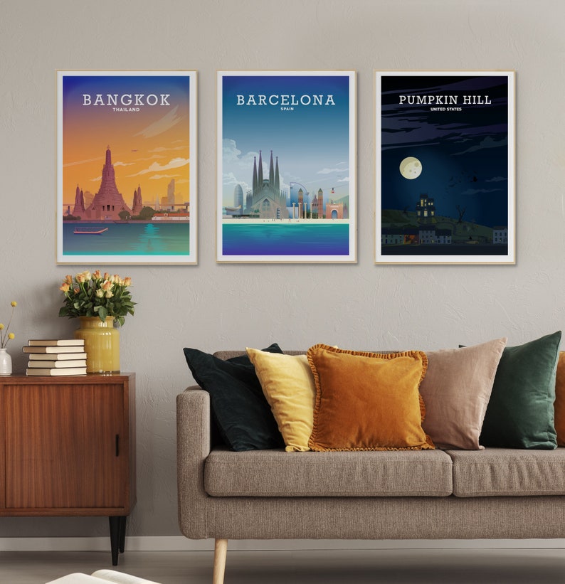 May include: Three framed city skyline posters with a minimalist design. The posters are hanging on a light gray wall above a gray couch with pillows. The posters feature the city skylines of Bangkok, Thailand, Barcelona, Spain, and Pumpkin Hill, United States.