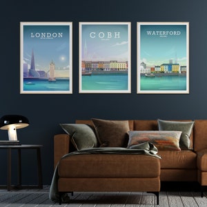 May include: Three framed city skyline prints with a blue background. The prints feature the cities of London, Cobh, and Waterford. The prints are hanging on a dark blue wall above a brown leather sofa.