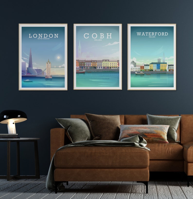 May include: Three framed city skyline prints with a blue background. The prints feature the cities of London, Cobh, and Waterford. The prints are hanging on a dark blue wall above a brown leather sofa.