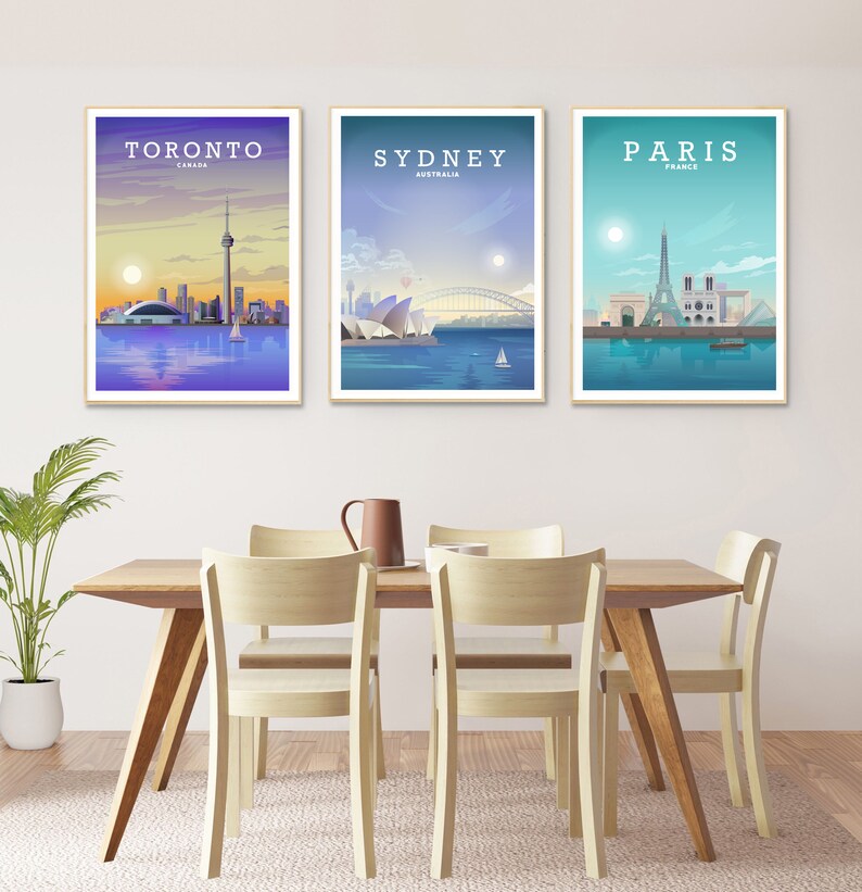 May include: Three framed city skyline posters with a white background. The posters feature Toronto, Canada; Sydney, Australia; and Paris, France. The posters are hanging on a white wall above a wooden dining table with four chairs.