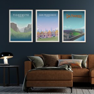 Pu&ograve; includere: Tre poster incorniciati su una parete blu scuro sopra un divano in pelle marrone. I poster mostrano illustrazioni del Parco Nazionale di Yosemite, delle Painted Ladies di San Francisco e di uno stadio di baseball a San Francisco.