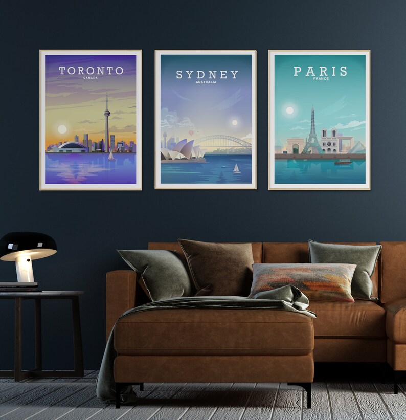 May include: Three framed city skyline posters with a brown leather sofa in the foreground. The posters feature the skylines of Toronto, Canada; Sydney, Australia; and Paris, France. Each poster has the city name and country name printed at the top.