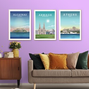 May include: Three framed prints of cityscapes. The prints are hung on a light purple wall. The prints feature illustrations of Alcatraz, Armagh, and Athens. Each print has the city name and location printed at the top.