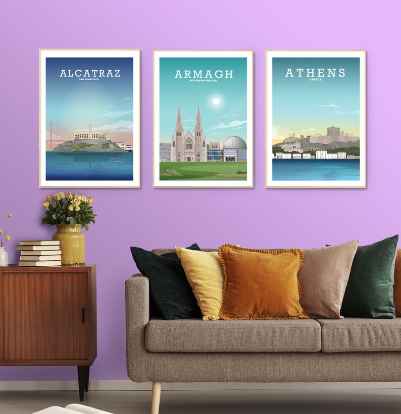 May include: Three framed prints of cityscapes. The prints are hung on a light purple wall. The prints feature illustrations of Alcatraz, Armagh, and Athens. Each print has the city name and location printed at the top.