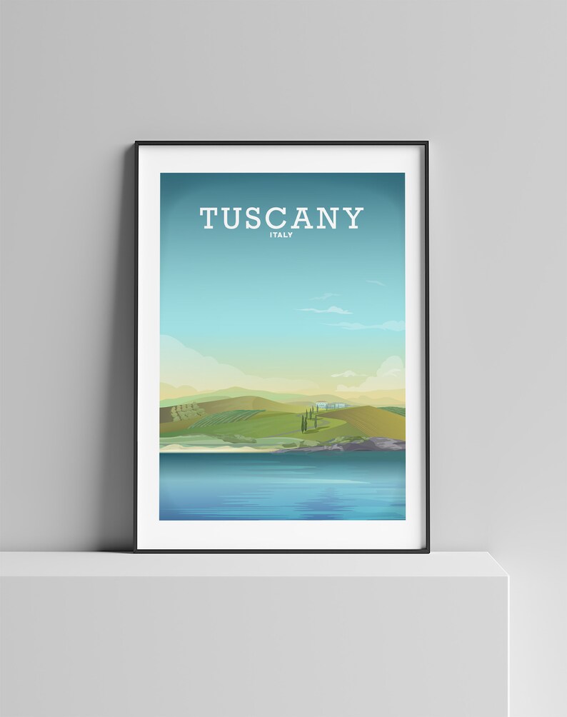 May include: A framed print with a landscape scene of rolling green hills, a blue lake, and a few trees. The text "Tuscany, Italy" is printed at the top of the print.