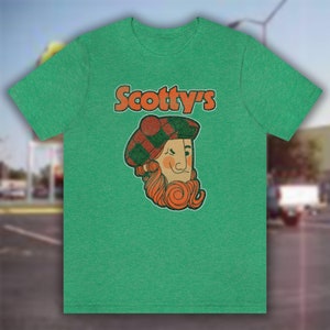 May include: Green t-shirt with a vintage-style logo for "Scotty's" featuring a cartoon man with a red beard and a plaid hat.