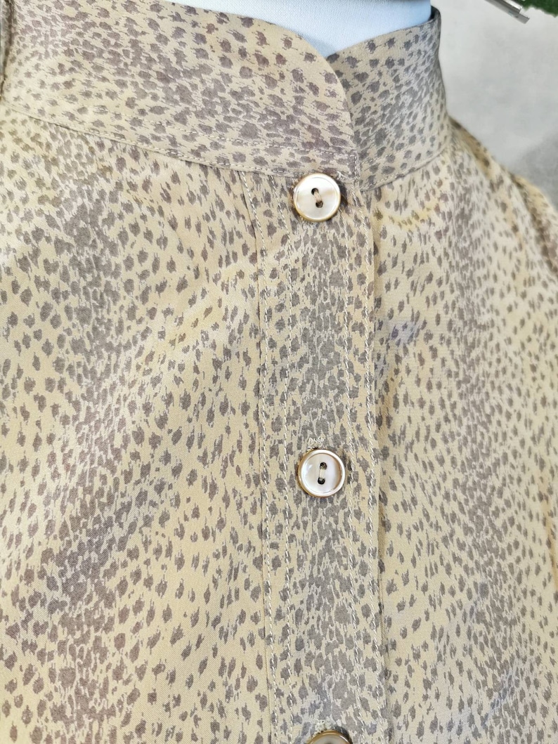 Op de afbeelding: Een beige overhemd met knopen en een bruine dierenprint. Het overhemd heeft een mandarijnkraag en een enkele knoopsluiting aan de hals.
